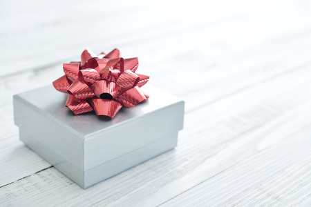 Silver gift box with red ribbon over white wooden backgroundの写真素材