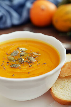 Bowl of pumpkin soup with decorative pumpkin on wooden backgroundの写真素材