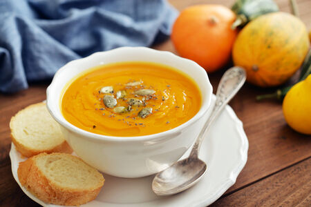 Bowl of pumpkin soup with decorative pumpkin on wooden backgroundの写真素材