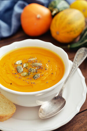 Bowl of pumpkin soup with decorative pumpkin on wooden backgroundの写真素材