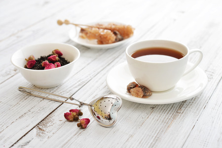 Cup of tea with dry rose buds and tea strainer in the shape of heartの写真素材