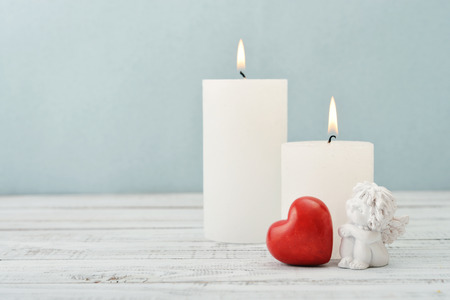 Statuette of small  angel with stone heart and candles over light backgroundの写真素材