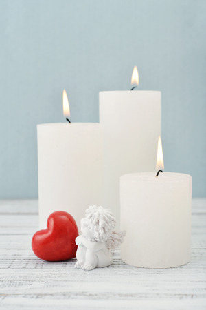 Statuette of small  angel with stone heart and candles over light backgroundの写真素材