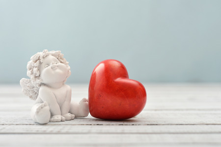Statuettes of small  angels with stone heart over light backgroundの写真素材