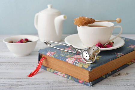 Cup of tea with dry rose buds and tea strainer in the shape of heartの写真素材