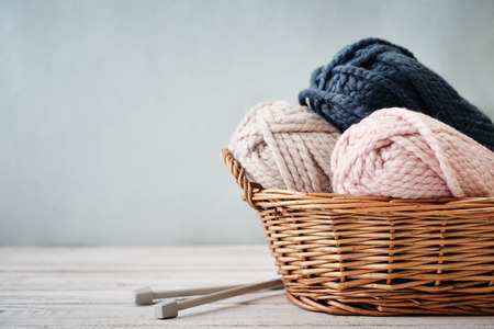 Wool yarn in coils with knitting needles in wicker basket on light blue backgroundの写真素材
