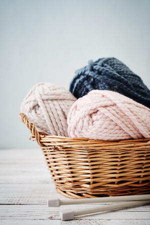 Wool yarn in coils with knitting needles in wicker basket on light blue backgroundの写真素材