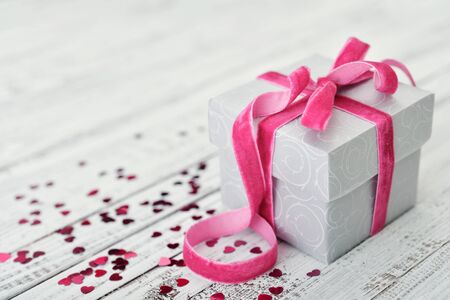 Gift box with pink bow and confetti in shape of heart on wooden backgroundの写真素材