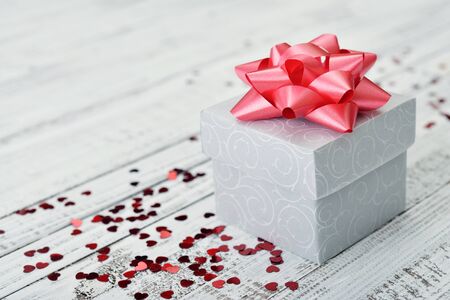 Gift box with red bow and confetti in shape of heart on wooden backgroundの写真素材