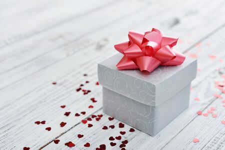 Gift box with red bow and confetti in shape of heart on wooden backgroundの写真素材