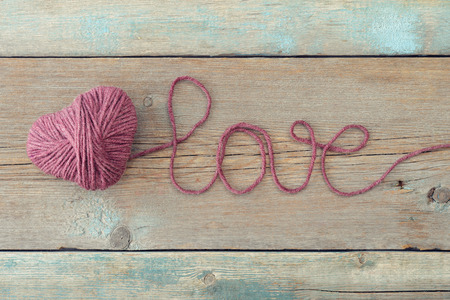 Pink clew in shape of heart and word "love"on vintage wooden backgroundの写真素材
