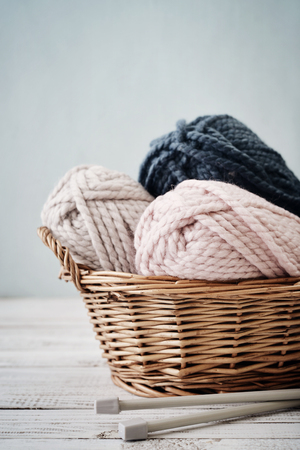 Wool yarn in coils with knitting needles in wicker basket on light blue backgroundの写真素材