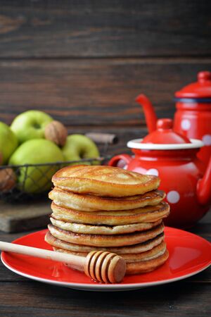 Stack of pancakes on plate with vintage teapots and fresh apples on wooden backgroundの写真素材