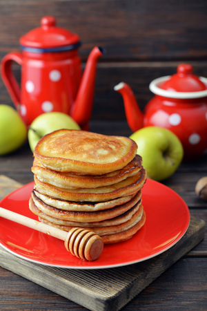 Stack of pancakes on plate with vintage teapots and fresh apples on wooden backgroundの写真素材