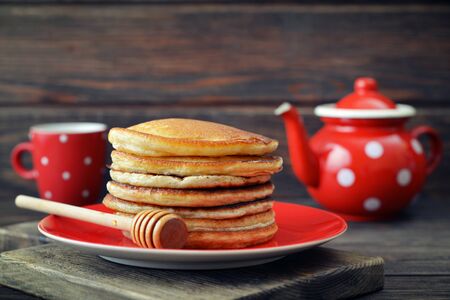 Stack of pancakes on plate with vintage teapots on wooden backgroundの写真素材