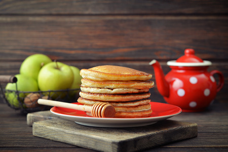 Stack of pancakes on plate with vintage teapots and fresh apples on wooden backgroundの写真素材