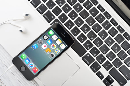KIEV, UKRAINE - JANUARY 29, 2015: Apple iPhone 5s and MacBook Air on table. Apple Inc. is an American multinational corporation that designs, develops, and sells consumer electronics.のeditorial素材