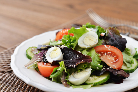 Salad mix with lettuce, tomato, cucumber and quail eggs in bowl on wooden backgroundの写真素材