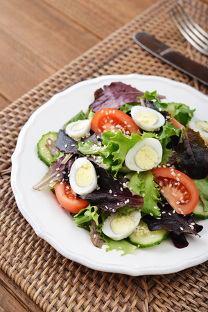 Salad mix with lettuce, tomato, cucumber and quail eggs in bowl on wooden backgroundの写真素材