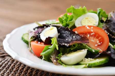 Salad mix with lettuce, tomato, cucumber and quail eggs in bowl on wooden backgroundの写真素材