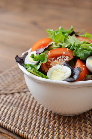 Salad mix with lettuce, tomato, cucumber and quail eggs in bowl on wooden backgroundの写真素材