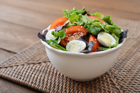 Salad mix with lettuce, tomato, cucumber and quail eggs in bowl on wooden backgroundの写真素材