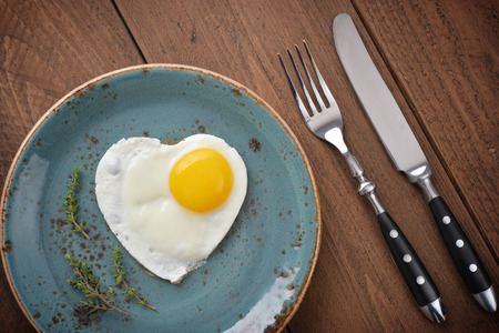 Fried egg in shape of heart on blue plate top viewの写真素材