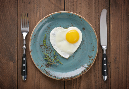 Fried egg in shape of heart on blue plate top view