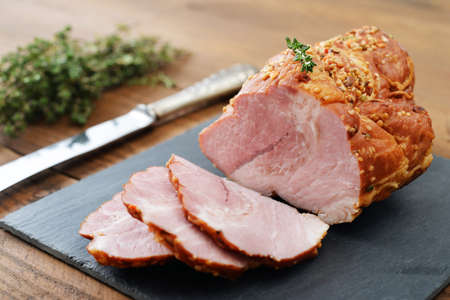 Sliced cold baked pork with herbs on a slate cutting board on wooden backgroundの写真素材