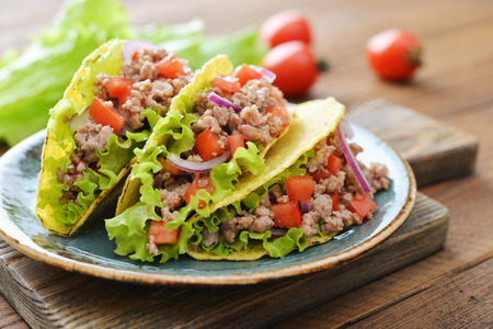 Mexican tacos with meat, onion and tomato on plate on wooden backgroundの写真素材