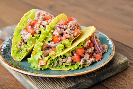 Mexican tacos with meat, onion and tomato on plate on wooden backgroundの写真素材