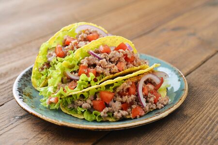 Mexican tacos with meat, onion and tomato on plate on wooden backgroundの写真素材