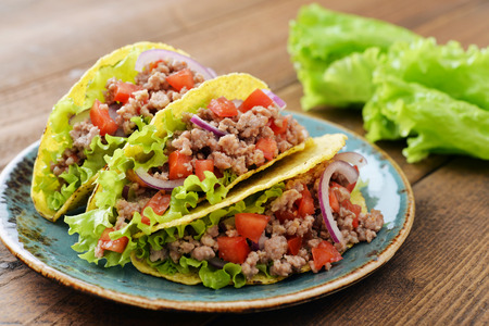 Mexican tacos with meat, onion and tomato on plate on wooden backgroundの写真素材