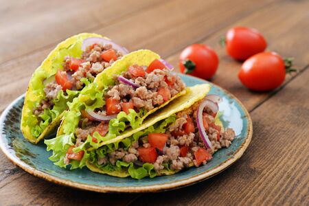 Mexican tacos with meat, onion and tomato on plate on wooden backgroundの写真素材