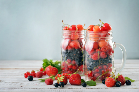 Different summer berries in glass jar with handle on wooden backgroundの写真素材