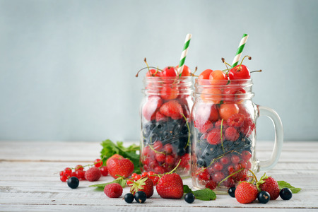 Different summer berries in glass jar with handle on wooden backgroundの写真素材