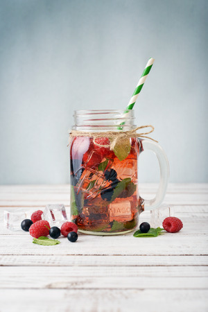 Lemonade with summer berries in glass jar with handle on wooden backgroundの写真素材