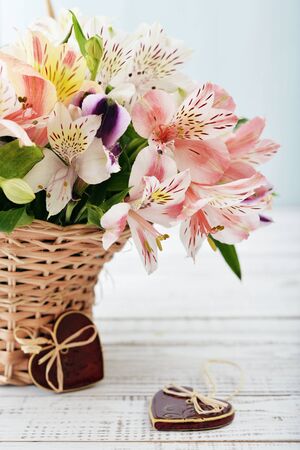Bouquet alstroemeria in wicker basket with ceramic hearts on light blue backgroundの写真素材