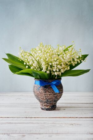 Bouquet of may-lily in vase on blue backgroundの写真素材