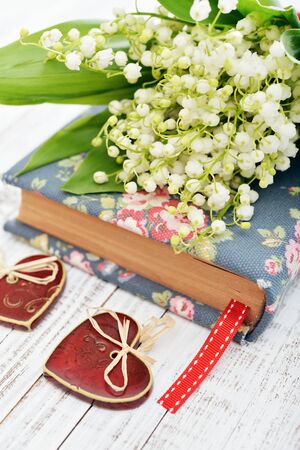Bouquet of may-lily with book closeup and ceramic heart on wooden backgroundの写真素材