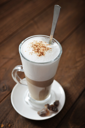Coffee in glass cup with cinnamon over wooden backgroundの写真素材