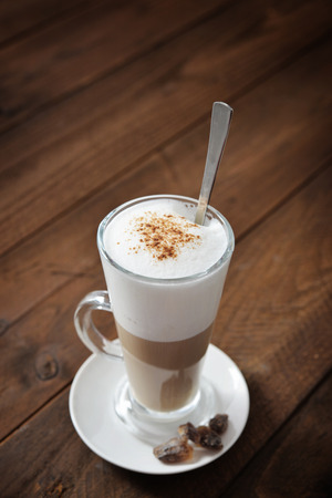 Coffee in glass cup with cinnamon over wooden backgroundの写真素材