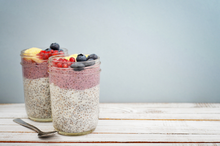 Pudding with chia seeds, yogurt and fresh fruits in glass jars on blue backgroundの写真素材