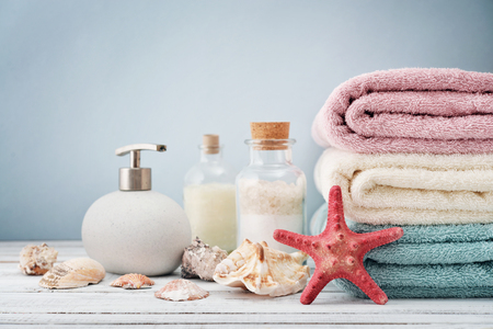 Soap dispenser with bottles of shampoo and sea salt with towels on light backgroundの写真素材