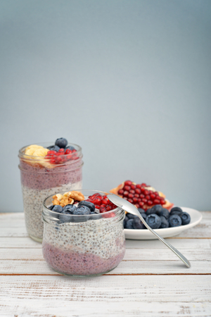 Pudding with chia seeds, yogurt and fresh fruits in glass jars on blue backgroundの写真素材