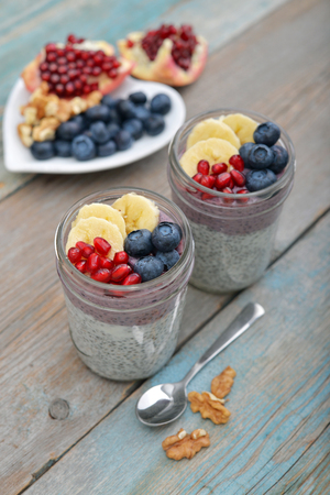 Pudding with chia seeds, yogurt and fresh fruits in glass jars on wooden backgroundの写真素材