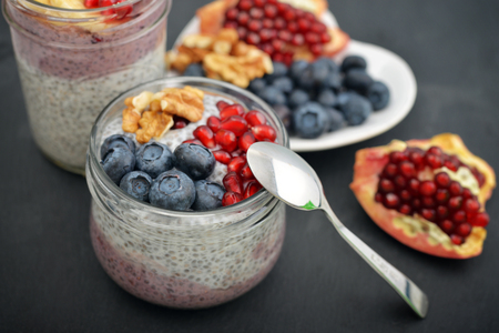 Pudding with chia seeds, yogurt and fresh fruits in glass jars on black backgroundの写真素材