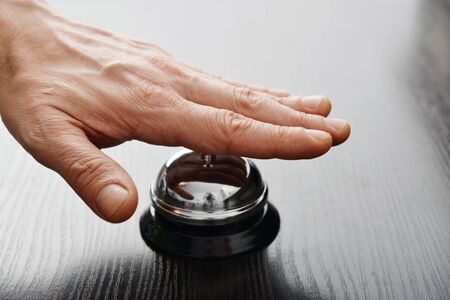 Male hand ringing in service bell on wooden table closeupの写真素材