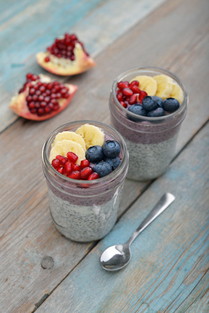 Pudding with chia seeds, yogurt and fresh fruits in glass jars on wooden backgroundの写真素材