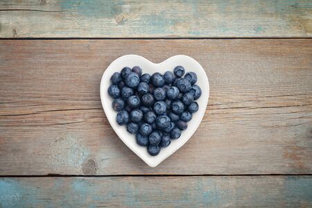 Plate in shape of heart with blueberries on wooden background, top viewの写真素材